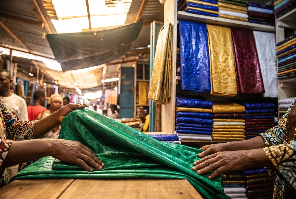 Market stall in Dakar stacked with folded bazin riche in indigo, gold and burgundy